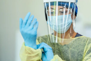 A healthcare worker wearing complete medical PPE, including disposable face shield, gloves, isolation gown, and surgical mask, ensuring full protection.