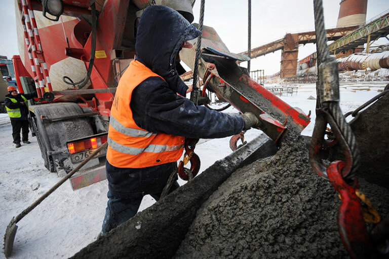 A worker fully equipped with PPE, including reflective gear, safety gloves, and boots, working by a concrete mixer, ensuring workplace safety.