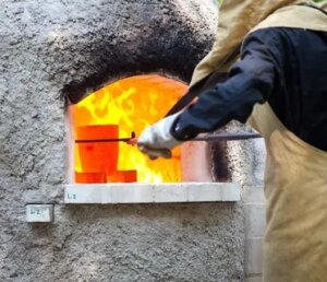 Worker in heat-resistant suit, gloves, and face/neck shield performing high-temperature work to prevent burns and injuries.